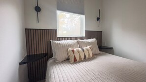 Ein Schlafzimmer mit einem großen Bett, zwei Nachttischen, einem Fenster mit Jalousien und Wandleuchten.