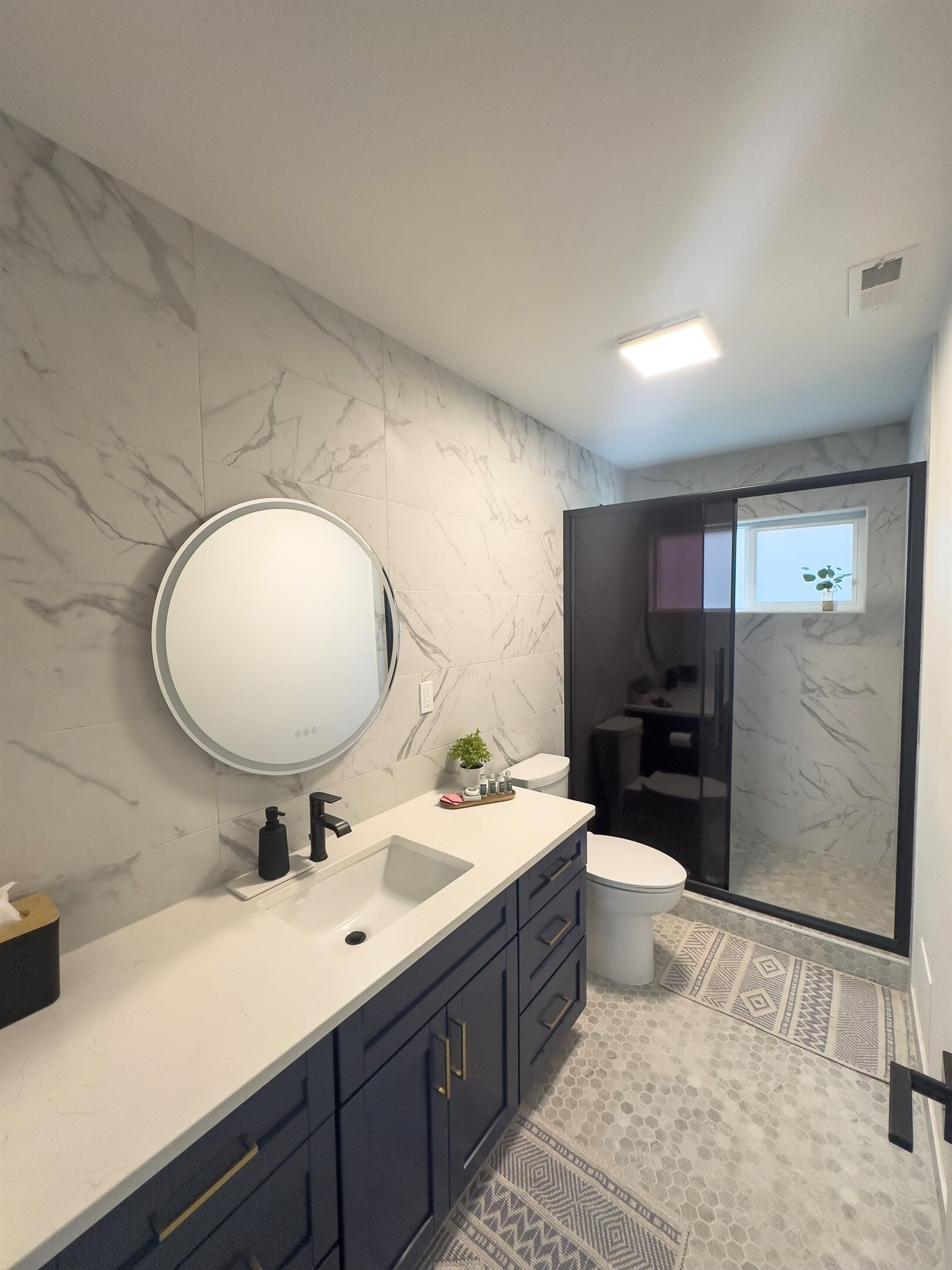 A modern bathroom with a marble backsplash, a round mirror, a sink, and a toilet.
