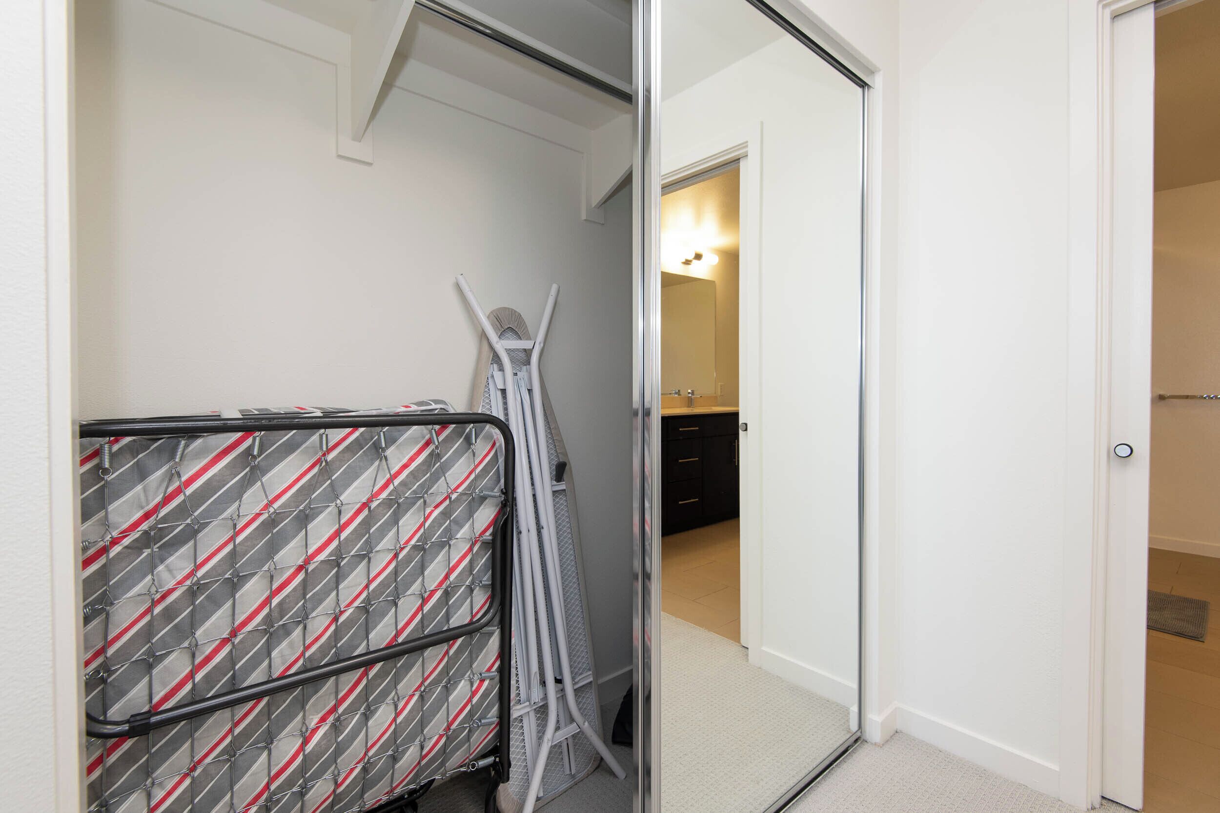 Une pièce dotée d’une porte coulissante donnant accès à une salle de bain, d’une chaise pliante en métal et d’une barrière en métal à motifs.