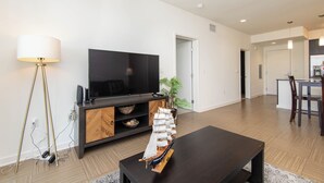 Een moderne woonkamer met een flatscreen televisie, een houten salontafel, en een eethoek met een tafel en stoelen.