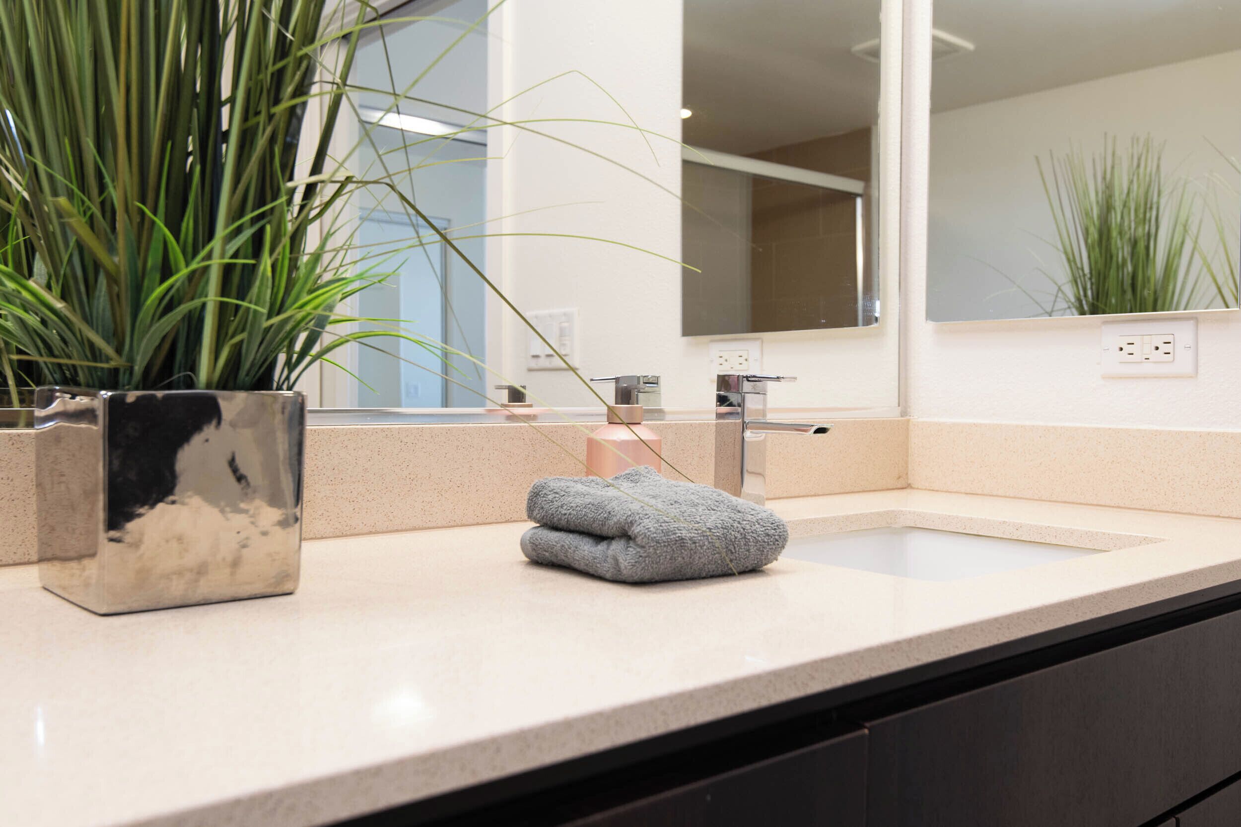 A bathroom with a large mirror, a sink, and a potted plant.