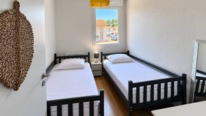 A room with two beds, a window with a view, a hanging light fixture, and a wall decoration.