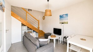 A living room with a sofa, TV, dining table, and a staircase.