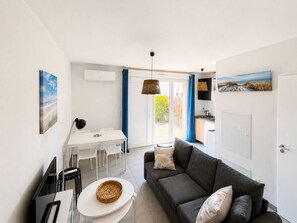 Una sala moderna con un sofá, una mesa de comedor con sillas, una zona de cocina y un ventanal corredero que da a un balcón.