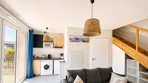 A modern apartment with a grey sofa, a washing machine, a microwave, and a dining area.