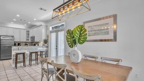 A modern kitchen with white cabinets, a stainless steel refrigerator, and a dining area with a wooden table and chairs. - Jack Chasin' Birdies (Destin)