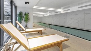 A modern indoor swimming pool area with lounge chairs and potted plants. - Central Haven Studio on Queen Street  (Auckland)
