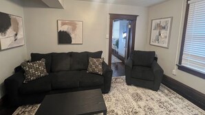A living room with a black sofa, a matching armchair, a coffee table, and abstract art on the walls. - Historic Downtown 1BR 2 Queens Near WVU & Dining (Morgantown)
