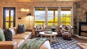 Un acogedor interior de cabaña con un sofá de cuero, dos sillones estampados, una mesa redonda de centro y una chimenea.