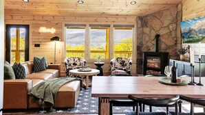 Un interior de cabaña acogedor, con chimenea de piedra, techo de madera y ventanas amplias que ofrecen vistas al exterior.