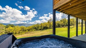 Un jacuzzi con vistas a un paisaje verdeado y árboles bajo un cielo despejado.