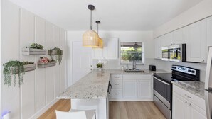 Eine moderne Küche mit weißen Schränken, einer Granitarbeitsplatte, einem eingebauten Backofen und einer hängenden Pendelleuchte.