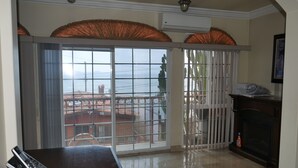 A room with a large sliding glass door leading to a balcony with a view of buildings and a body of water. There is a fireplace and a bottle of cleaning product on the floor. - Beautiful Ocean View Home In San Antonio del Mar (Tijuana)