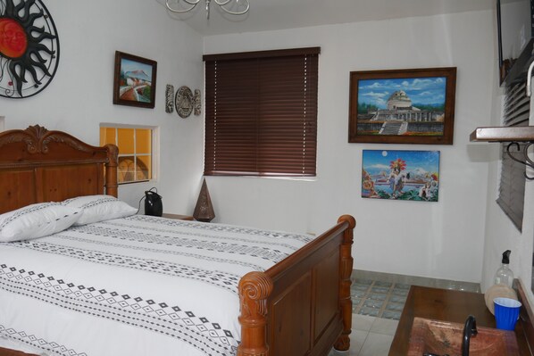 Un dormitorio con una cama de madera, una ventana con persianas y varios adornos en las paredes, incluyendo cuadros enmarcados.