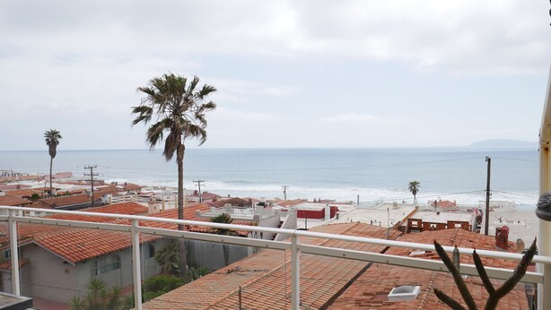 A residential area with red-tiled roofs, a palm tree, and a view of the beach and ocean. - Beautiful Ocean View Home In San Antonio del Mar (Tijuana)