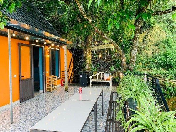 Un patio al aire libre con una mesa de comedor y sillas, un banco y una pequeña zona de estar con luces colgantes.
