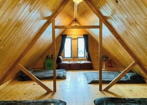 A triangular attic room with wooden beams, a bed, a window, and a fan. - 3Nai House Tam Dao (Tam Dao)