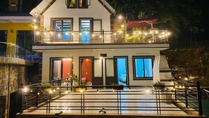 Un edificio de dos pisos con balcón, iluminación exterior y plantas en macetas.