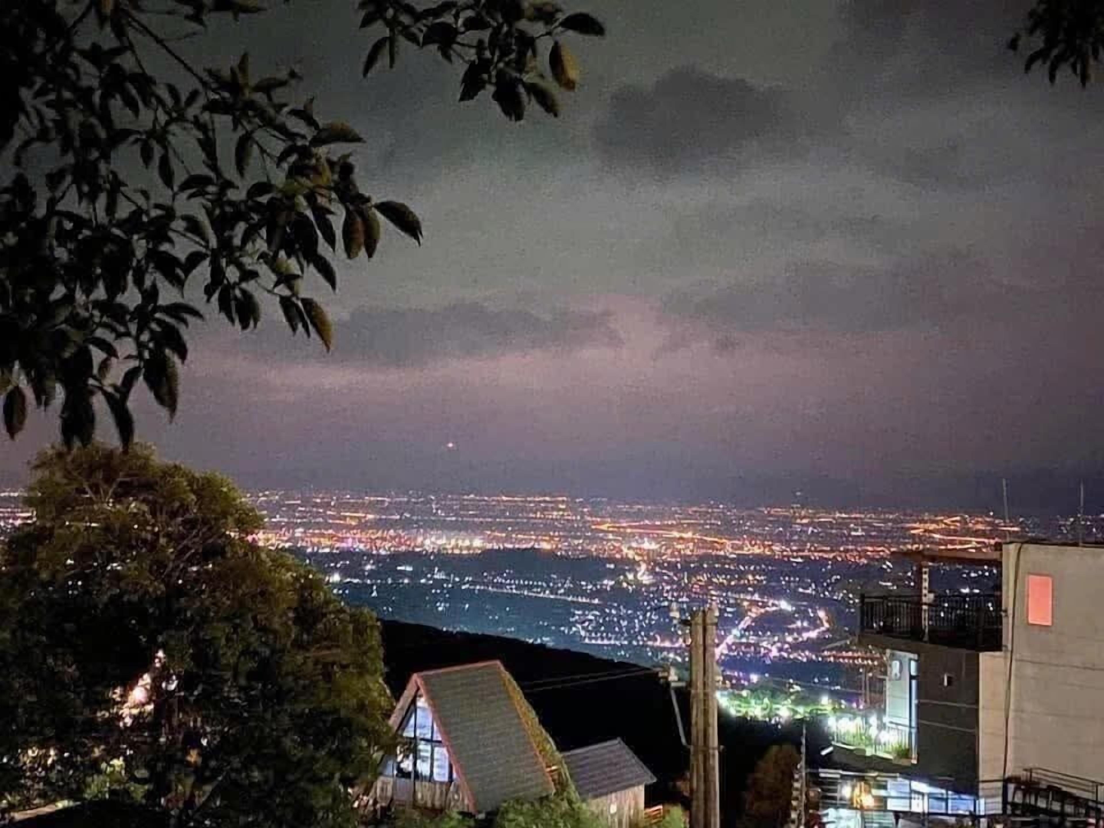 Visão noturna da cidade com prédios iluminados e horizonte urbano ao longe.