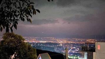 Visão noturna da cidade com prédios iluminados e horizonte urbano ao longe.