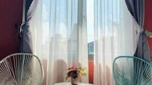 Una habitación con ventana, dos sillas y una mesa con un jarrón de flores.