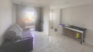 A modern living room with a sofa, a small table, and a kitchen area with a sink and cabinets. - Fairs and Shopping 202 (Vila Maria Alta São Paulo)