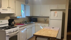 Una cocina con armarios blancos, estufa, microondas, refrigerador y una isla de madera.