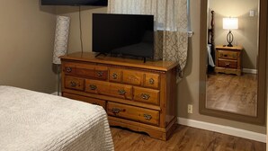 Un dormitorio con cama, cómoda, televisor, ventilador de techo y espejo.