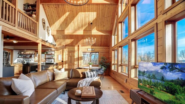 Un interior de cabaña espacioso, con un amplio salón, paredes de madera y un televisor que muestra un paisaje pintoresco.