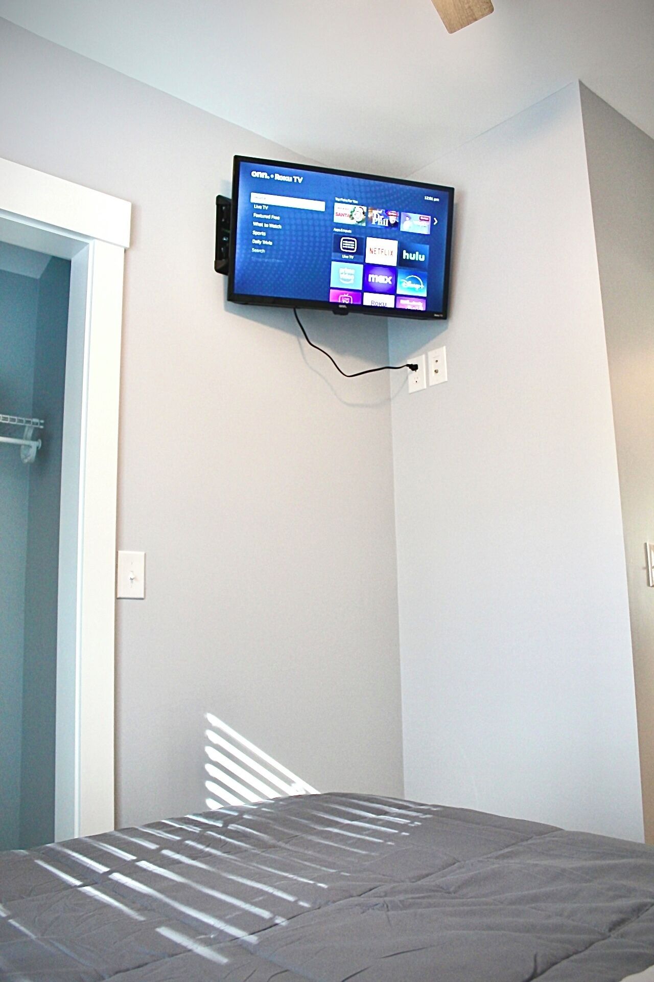 Une chambre à coucher avec un lit, un téléviseur fixé au mur qui permet d’accéder à des services de diffusion en continu, et une porte qui donne sur une autre pièce.
