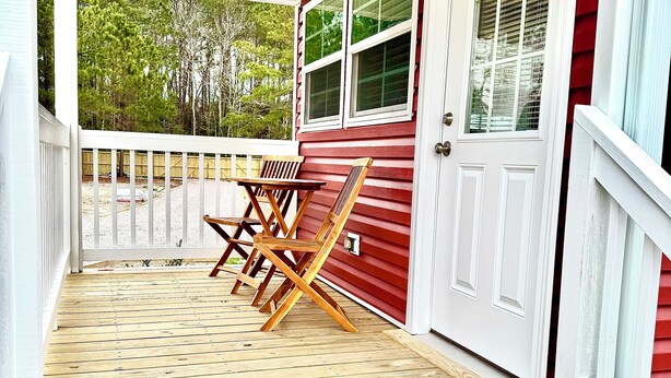 A wooden deck with two wooden chairs and a table, a white door, and a red exterior wall.