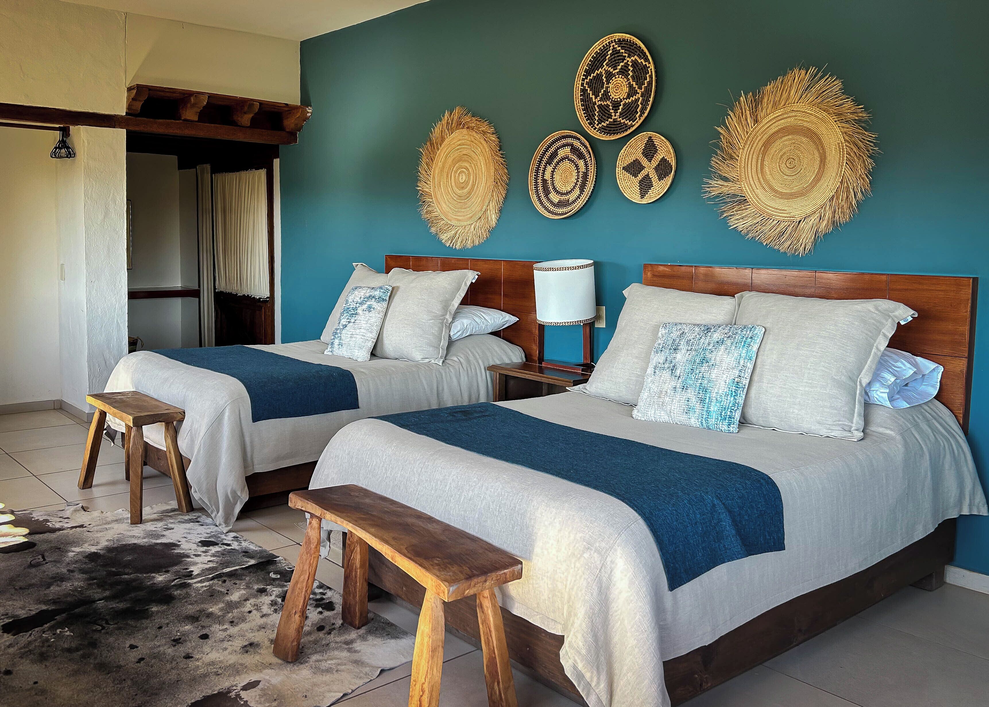 Habitación de hotel con dos camas, cabeceros de madera y una mesita de noche con una lámpara.