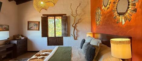 Ein gemütliches Schlafzimmer mit Bett, Nachttisch, Lampe und einem wandmontierten Spiegel.