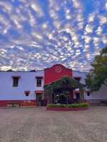 Un edificio con fachada roja y blanca, un arco central y un patio con plantas en macetas.