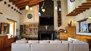 A cozy living room with a fireplace, wooden shelves with bottles, a large sofa, and a wooden staircase. - El Mesón del Ticúz Tapalpa (Tapalpa)
