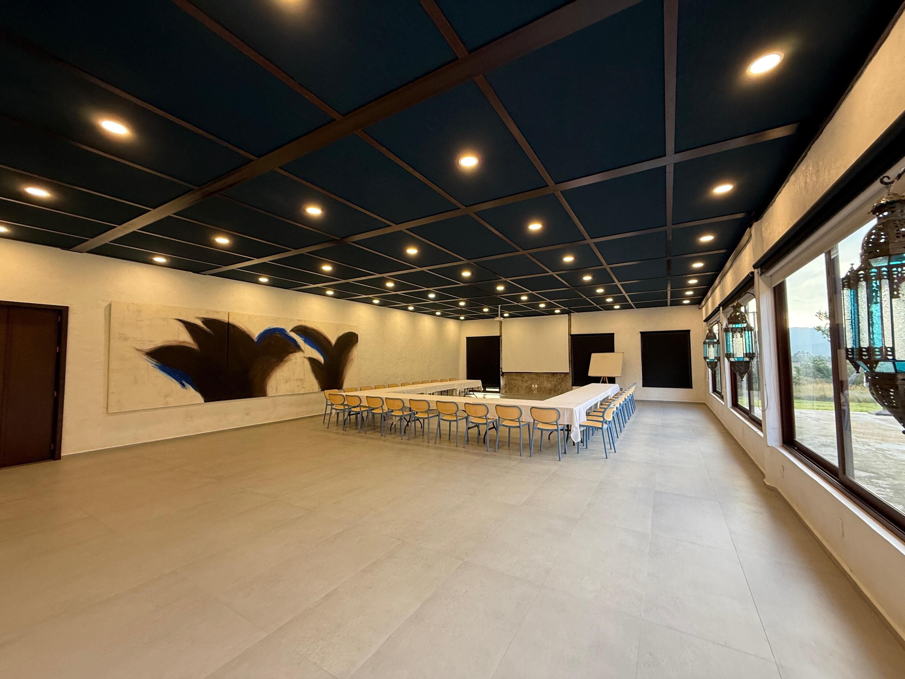 Un salón de conferencias con una larga mesa, sillas y un cuadro abstracto grande en la pared.