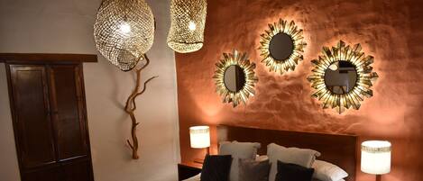 Ein helles Schlafzimmer mit einem großen Bett, zwei Nachttischen, einer hölzernen Bank und dekorativen Wandspiegeln.