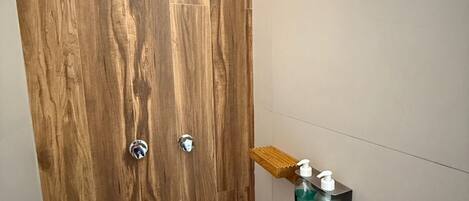 Baño con puerta de madera, zona de ducha y estante con artículos de aseo.