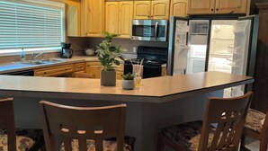A kitchen with wooden cabinets, a stainless steel refrigerator, a microwave, and a stove. There is a small island with chairs and a potted plant. - Cozy farmhouse in charming Great Falls with WiFi, AC and indoor parking (Great Falls)
