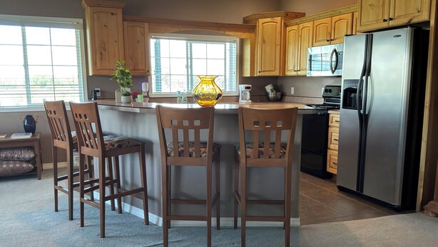 A kitchen with wooden cabinets, a stainless steel refrigerator, a central island with chairs, and a window providing natural light. - Cozy farmhouse in charming Great Falls with WiFi, AC and indoor parking (Great Falls)