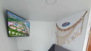 A small, modern room with a grey sofa, a small table with a bowl and a remote control, and a TV displaying a scenic view.