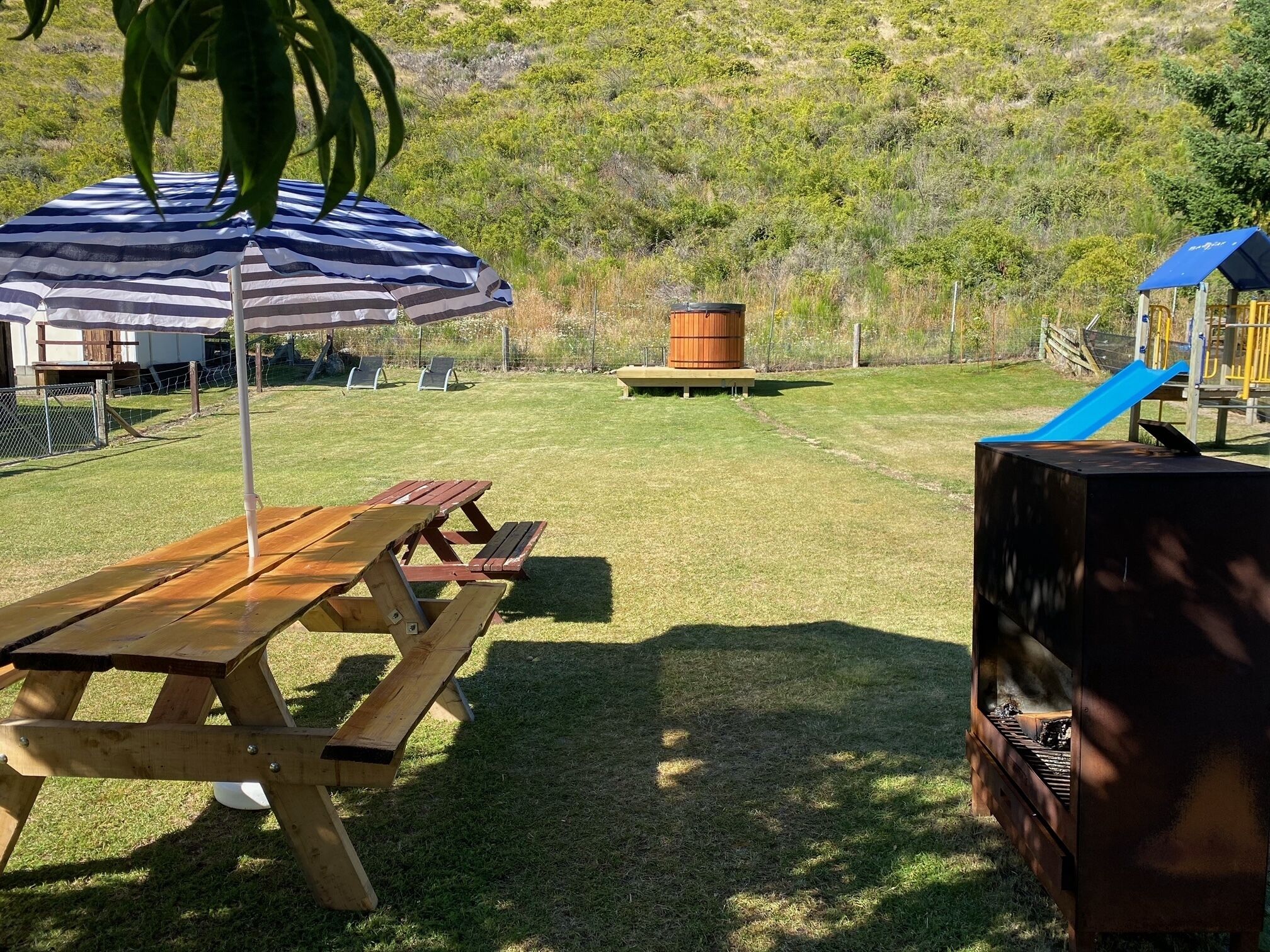 A picnic area with a wooden table and benches, a barbecue grill, and a playground with a slide.