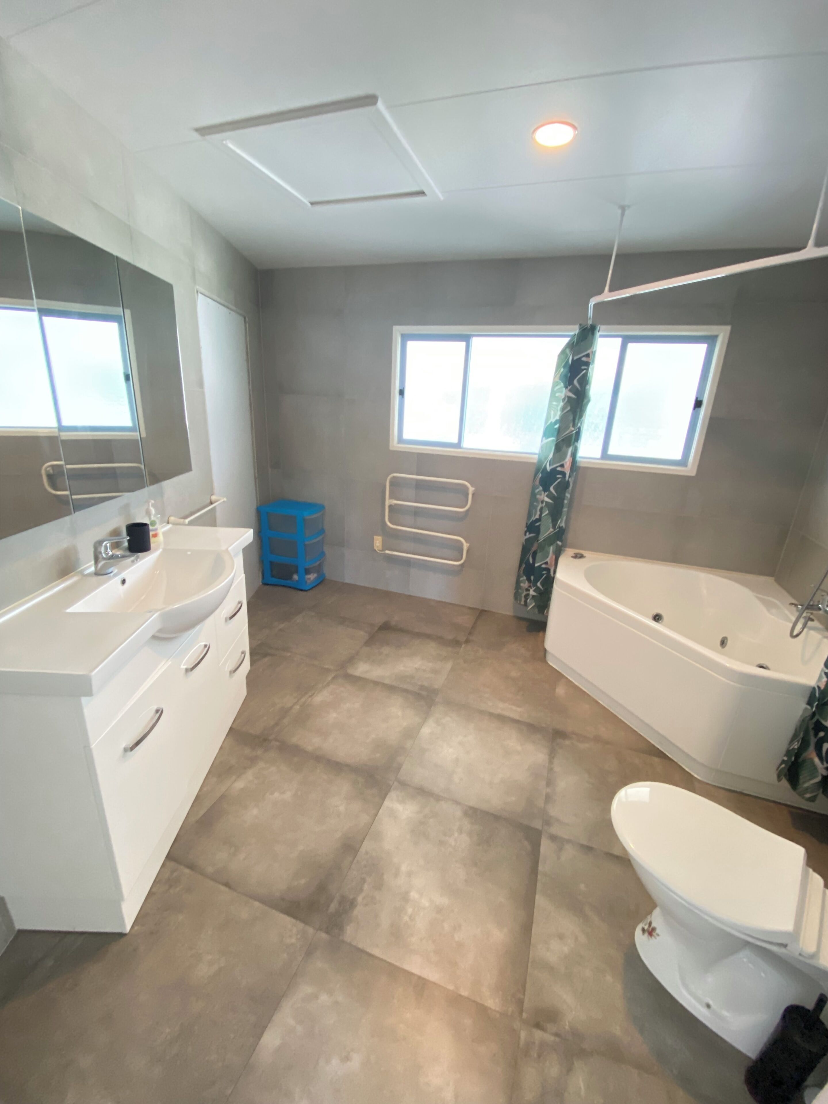 Un baño moderno con una bañera grande, un inodoro y un tocador con espejo. Dos ventanas proporcionan luz natural.