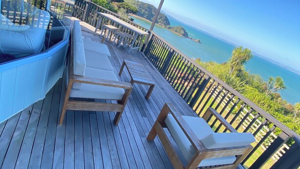Eine Holzterrasse mit Liegestühlen und einem Glasgeländer mit Blick auf die Küste.