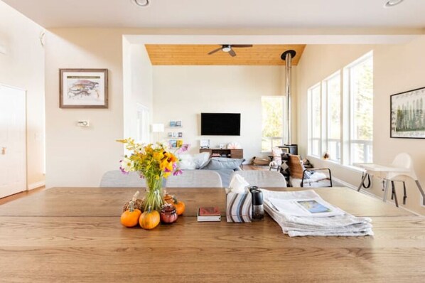 Un salon moderne avec une table à manger en bois, un canapé et un téléviseur. Il y a des fenêtres qui laissent entrer la lumière naturelle et un ventilateur de plafond.