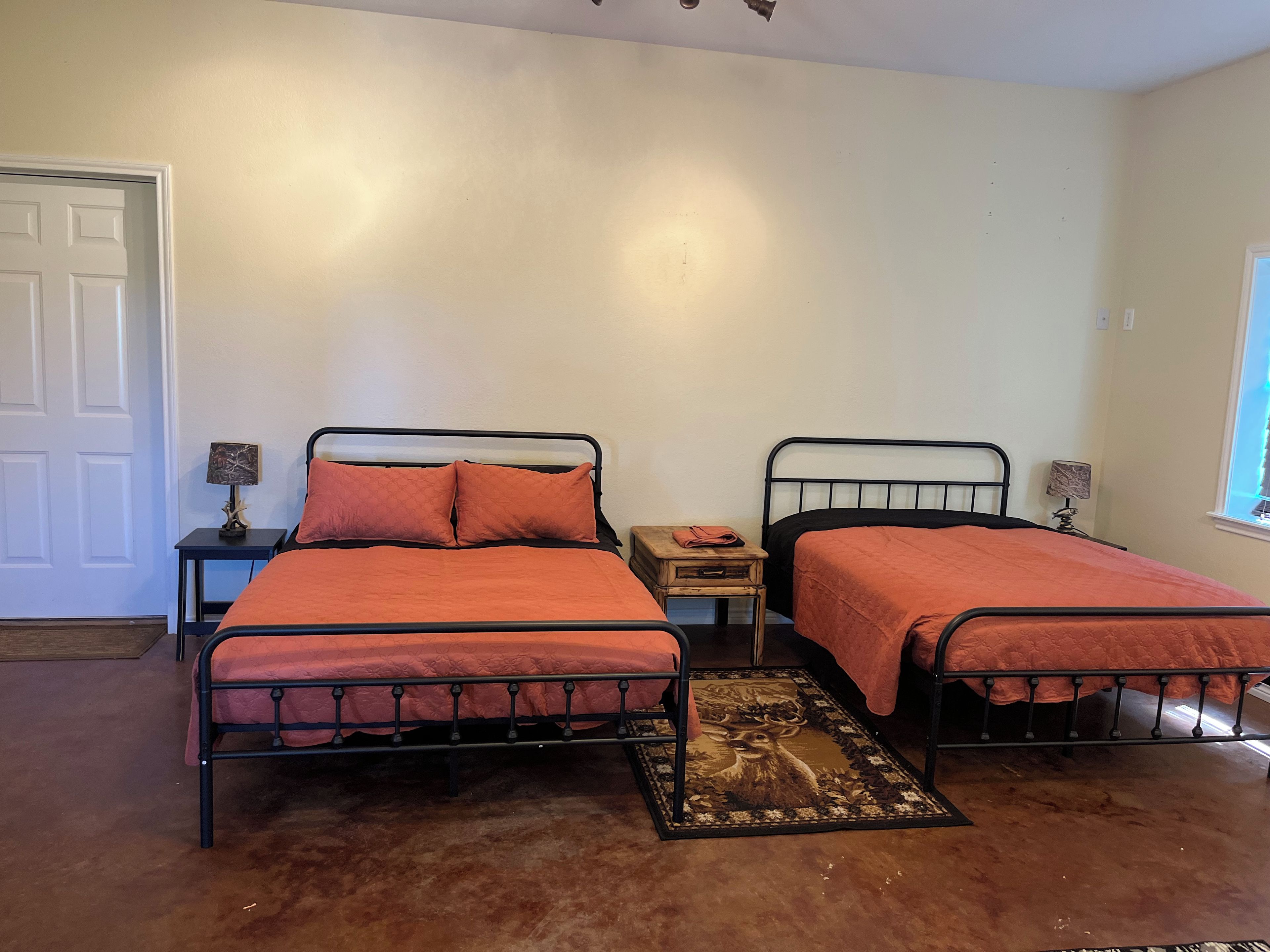 A bedroom with two metal beds, a small wooden nightstand, a lamp, and a window.