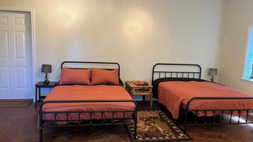 A bedroom with two metal beds, a small wooden nightstand, a lamp, and a window.