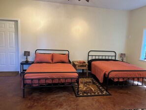 Un dormitorio con dos camas de metal, una mesita de noche de madera, una lámpara y una ventana.