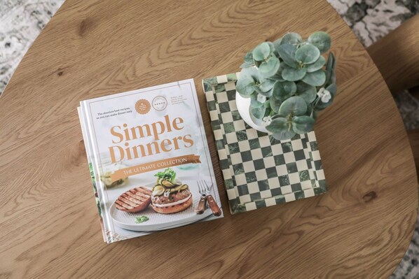 A book titled 'Simple Dinners' on a round wooden table with a checkered placemat and a small potted plant. - Stylish and Spacious Launceston Villa + Free Wifi (Launceston)