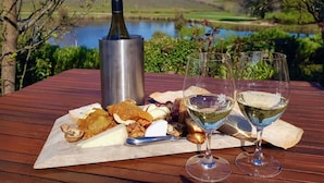 A wooden table with a bottle of wine, two glasses, and a cheese platter with various cheeses and nuts.